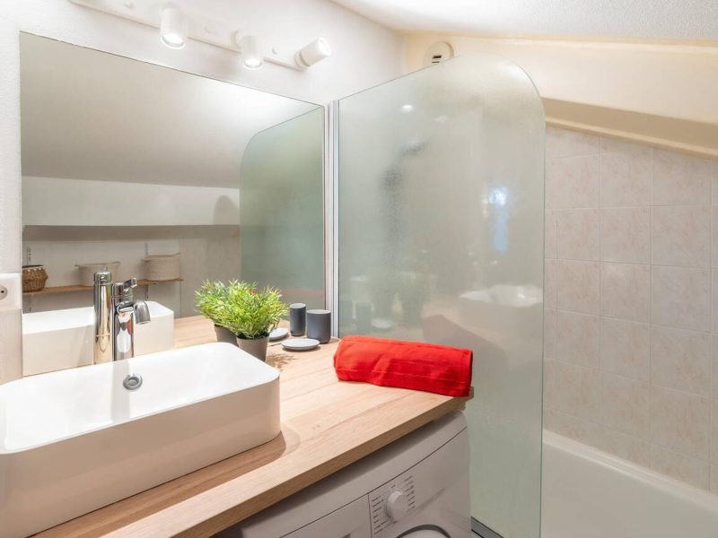 Domácí koupelna, nový světlý interiér koupelny s obloženou skleněnou sprchou, umyvadlovou skříňkou, interiérem navrženým s pračkou